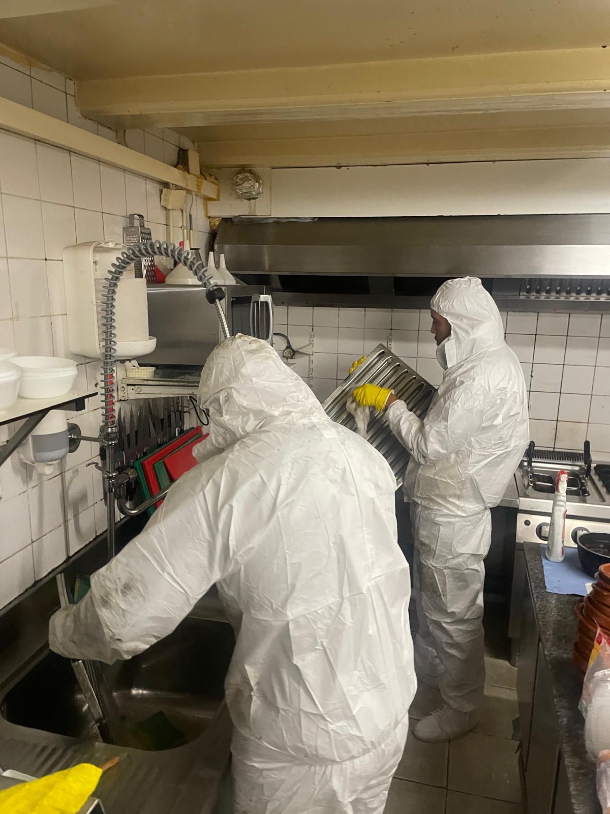 Team in beschermende kleding reinigt keukenapparatuur