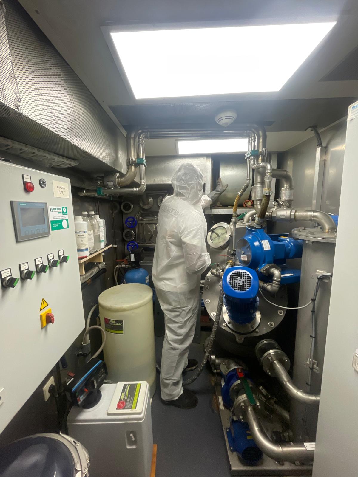 Monteur in beschermend pak inspecteert ventilatie-installatie in technische ruimte